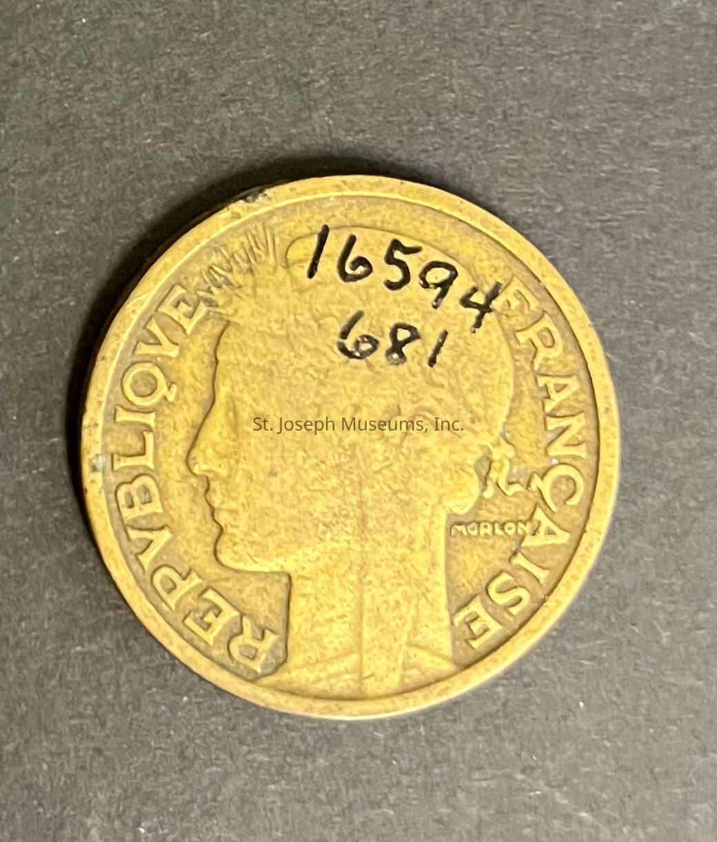 The image shows a French coin featuring an engraved profile of a person facing left, surrounded by the inscription "REPUBLIQUE FRANCAISE." The intricate details of the engraving highlight the artistic craftsmanship of the time. On the right side of the face, the word "MORLON" is subtly written, possibly indicating the designer or engraver. The coin carries a warm, golden color, suggesting it may have been made of brass or a similar alloy. The intricate details and historical context of the coin may be of keen interest to collectors and numismatists.
