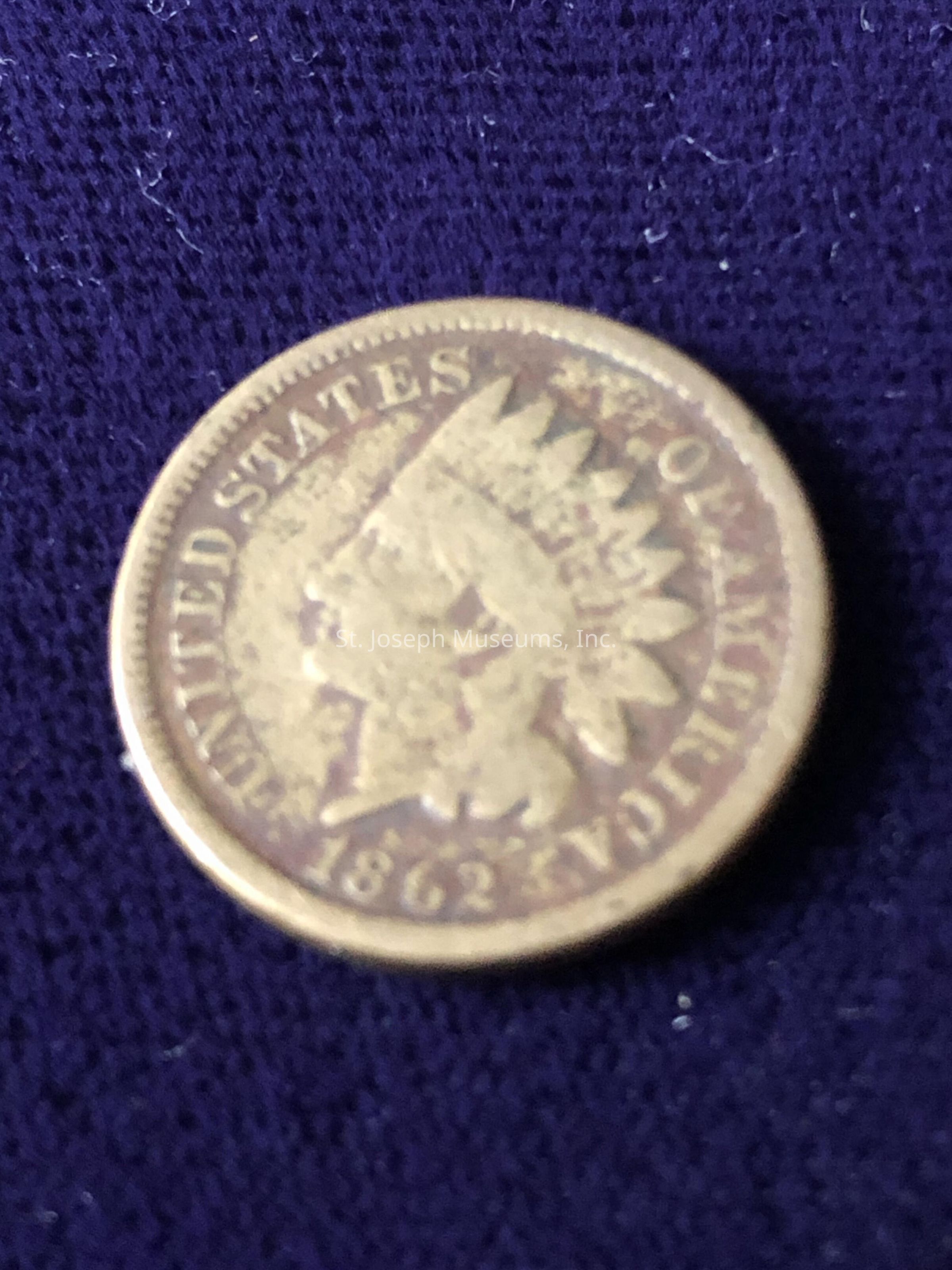 The image shows a United States coin, specifically the Indian Head cent, dated 1862, which prominently features the profile of a person wearing a Native American headdress on the obverse side, the coin itself is characterized by a worn appearance indicating age, with visible inscriptions surrounding the central image that read "UNITED STATES OF AMERICA," while at the bottom, the year "1862" is clearly engraved; the intricate design and historical context make the coin a significant piece of numismatic interest, reflecting a time when the theme of the Native American figure was common in currency, aiming to convey a sense of exploration and the frontier spirit during the mid-19th century, an era rich in cultural and historical developments, all encapsulated in the singular image of this small, round metallic object that has survived through numerous decades, capturing a story and offering a tangible connection to the distant past, providing both collectors and history enthusiasts with