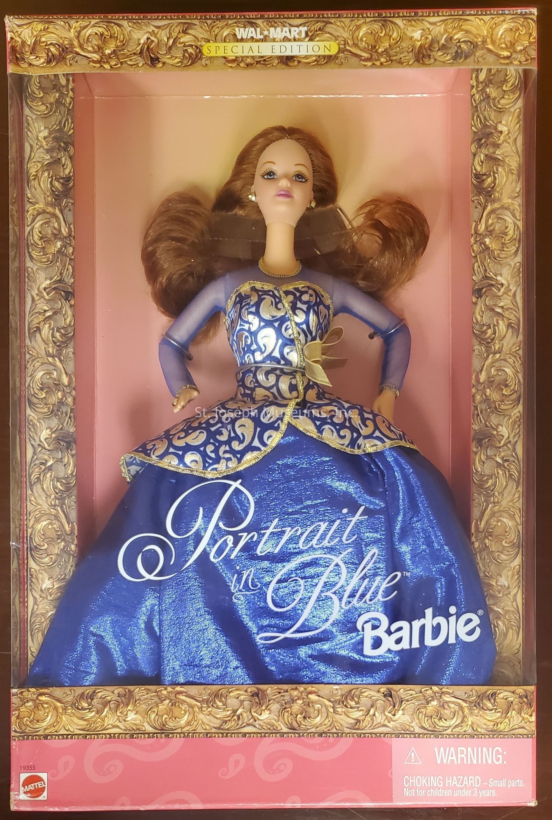 The image shows a "Portrait in Blue" Barbie doll encased in a box adorned with ornate, golden, frame-like designs. This Walmart Special Edition features Barbie wearing an elegant, long blue gown with intricate golden patterns, conveying a sense of regal elegance. Her hair is styled in voluminous waves, complementing the sophisticated aura of the doll. The packaging highlights the words "Portrait in Blue," emphasizing the doll's luxurious aesthetic. It's marked with Mattel branding, and a warning indicates a choking hazard for small parts, making it unsuitable for children under three years of age.