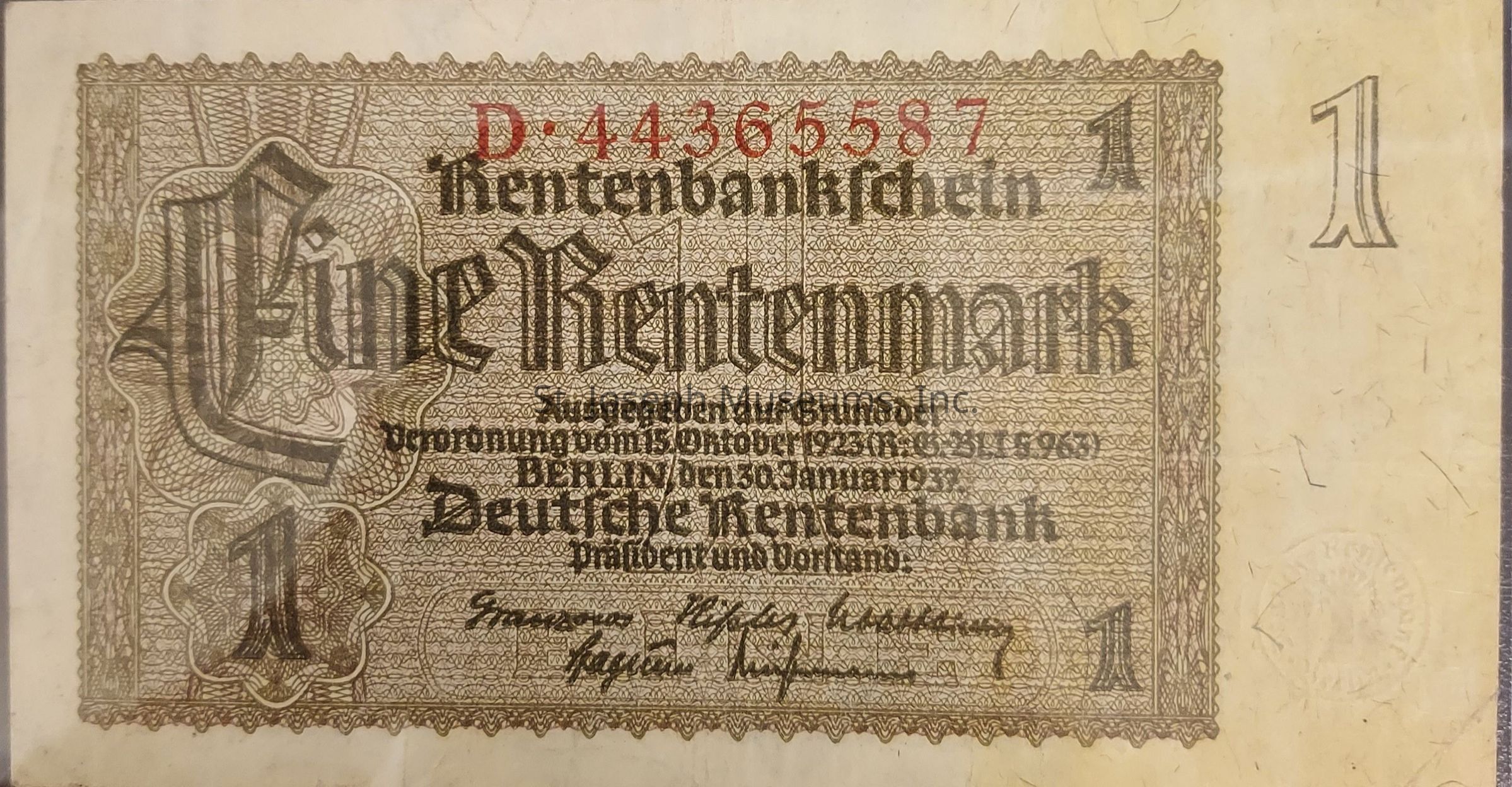The image depicts a historical German banknote known as the Rentenmark, denoted by the large "Eine Rentenmark" inscription in an ornate Gothic font across the note. The serial number "D-44365587" is prominently displayed at the top in red ink. The document outlines issuance details, noting "Berlin den 30 Januar 1923," indicating its date and place of issue. Surrounding the central text is a complex pattern of intricate decorative borders. Also visible are the number "1" in two corners, emphasizing the denomination. The bottom portion features signatures and the text "Deutsche Rentenbank," referring to the authority that issued the currency. The note's design and typography reflect the period's aesthetic and economic context.