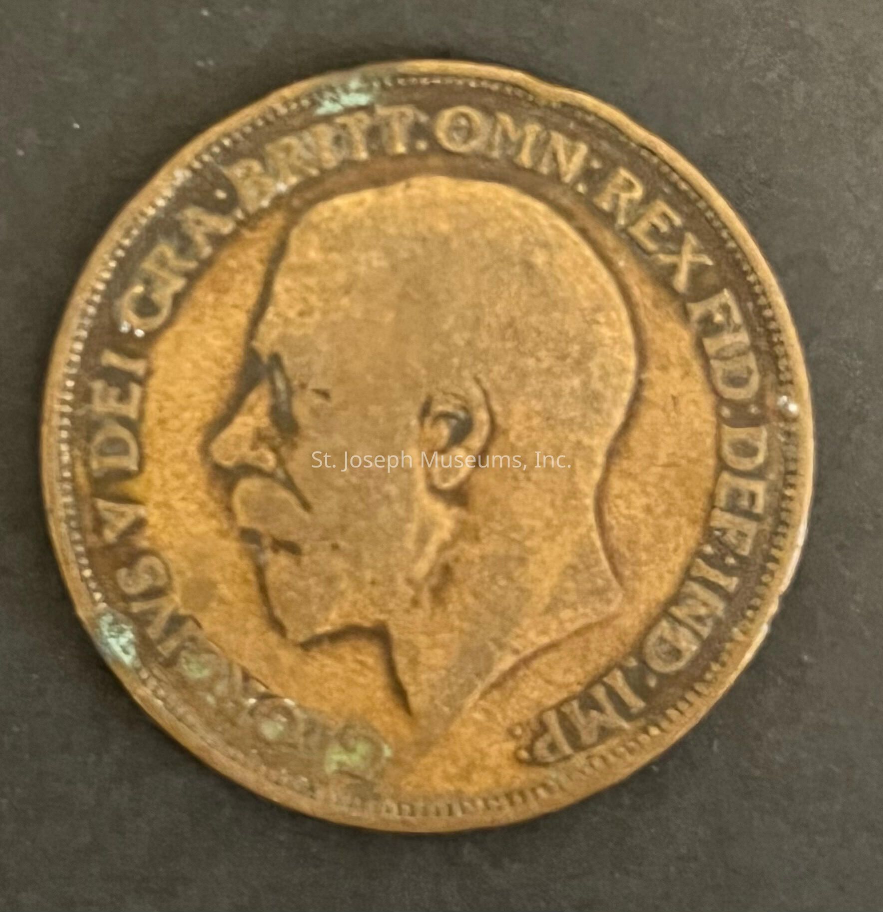 The image features an old coin with a portrait in profile on one side, featuring a male figure wearing minimal adornments. The inscriptions around the edge read, in part, "BRITT: OMN: REX FID: DEF: IND: IMP," highlighting its British origin. The coin is worn, suggesting it might have significant age and history. The surface of the coin displays a patina, indicating oxidation over time, which adds to its antique appearance and suggests it might have been in circulation for many years. The detailed craftsmanship reflects the intricate designs typical of historical coins.