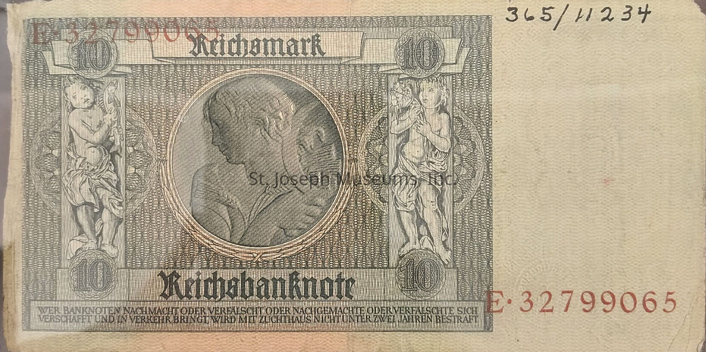 The image shows a historical 10 Reichsmark banknote featuring intricate designs and motifs. In the center, there is a circular portrait of a woman, and on either side, two ornate figures are depicted, possibly representing cherubs or similar mythological beings. The denomination "10" is prominently displayed within circular medallions at the top corners and the bottom corners adjoining the word "Reichsbanknote" printed in a bold, black Gothic font. Surrounding the central imagery is a detailed, fine-lined pattern providing texture and depth to the banknote. The serial number is printed in red ink at the bottom right corner, reading "E·32799065," while the top right corner holds, emphasizing the vintage appearance of the currency. Below the main elements, there is a statement warning against the forgery of banknotes, characteristic of the period's financial measures to ensure authenticity and