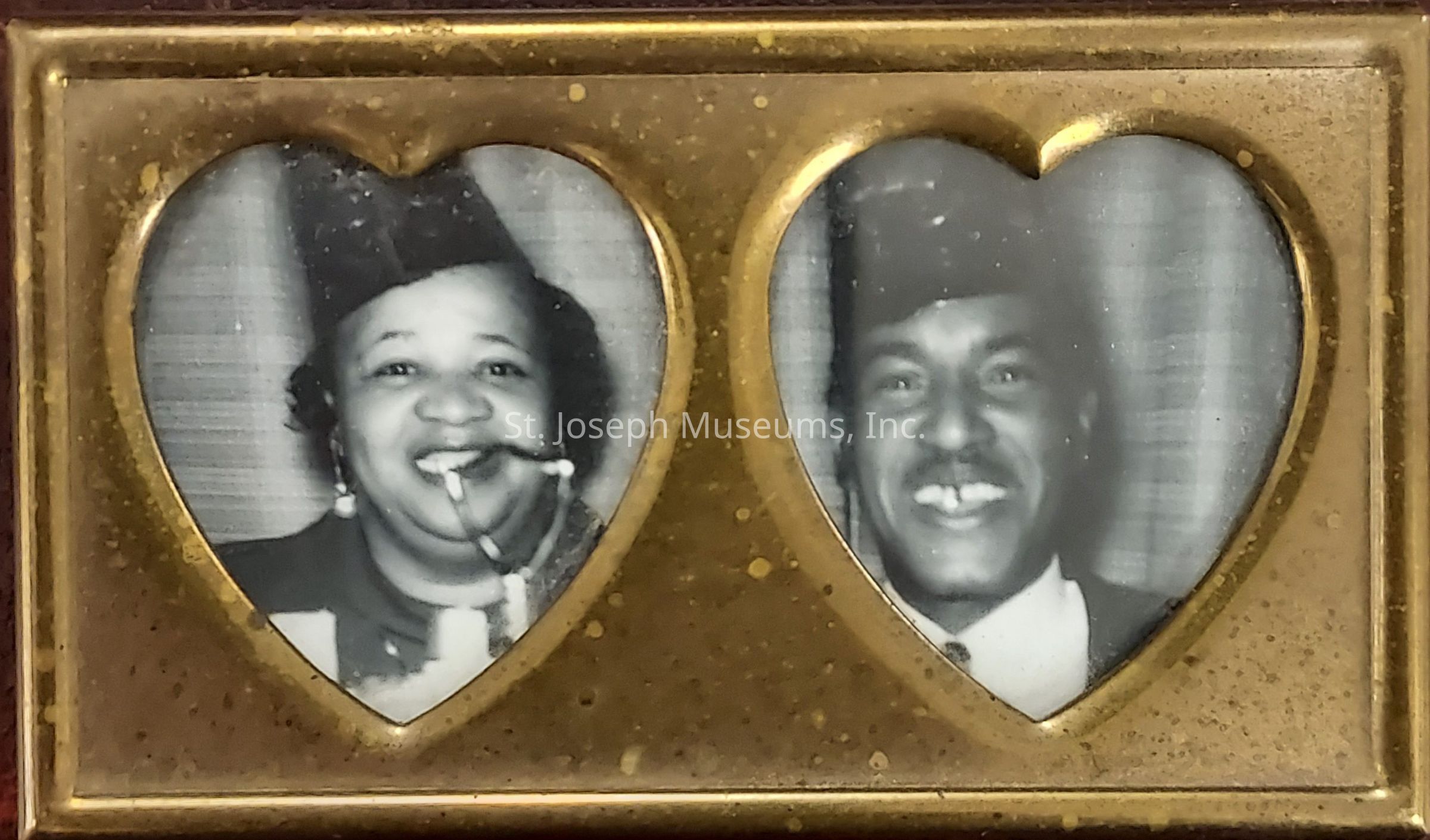 The image shows a pair of black-and-white photographs framed within heart-shaped openings in a gold-colored frame, each featuring a smiling person wearing a fez hat; the person on the left, a woman, appears to be smoking a pipe and is wearing earrings, while the person on the right is a man, both exuding a joyful and lighthearted aura, captured in what looks like a vintage or nostalgic setting, with the overall ambiance conveying a sense of warmth, affection, and perhaps a cherished memory preserved through time, emphasizing the bond shared between the two individuals displayed side by side.