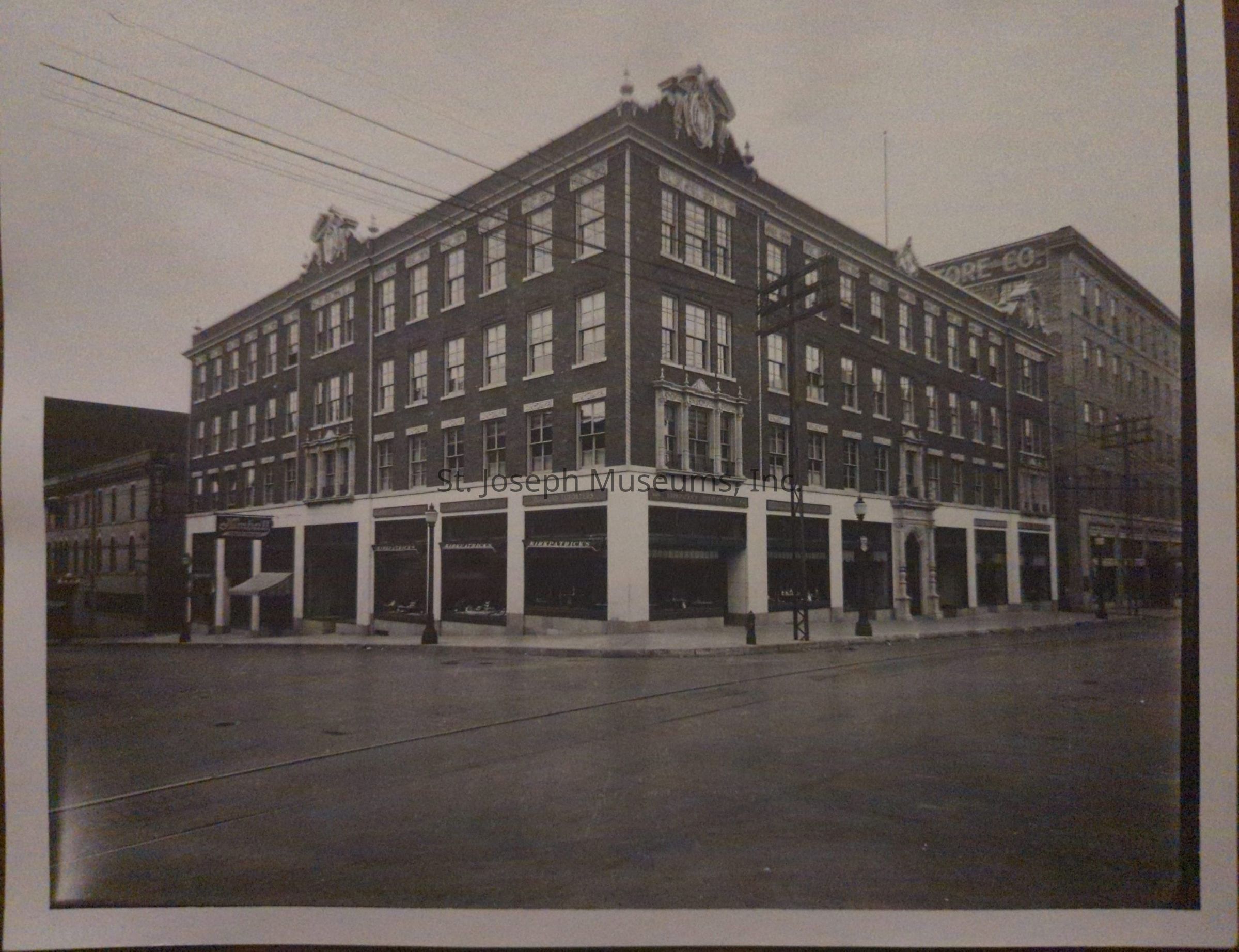 Black-and-white photograph depicting the Kirkpatrick building at the corner of 7th and Francis Street, showcasing a multi-story brick structure with decorative architectural elements. The building's facade features large windows and distinct entries, while the surrounding streets are quiet and show early 20th-century urban character.