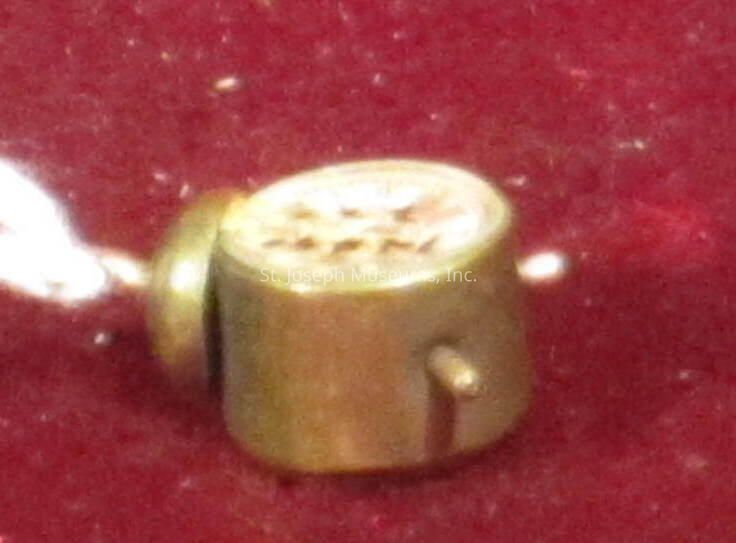 The image depicts a small, cylindrical brass object. The object features a textured top with a pattern of small holes, possibly for functionality or decoration. There is a protrusion or knob on the side, suggesting it may have a specific use, like a connection or fastening purpose. The background contrasts with the shiny, metallic appearance, enhancing the visibility of the item. The image might have been taken in close-up, focusing on the object’s details. The lighting highlights its polished surface, creating reflective spots that emphasize its metallic nature. The overall impression is of a finely crafted, possibly functional object.