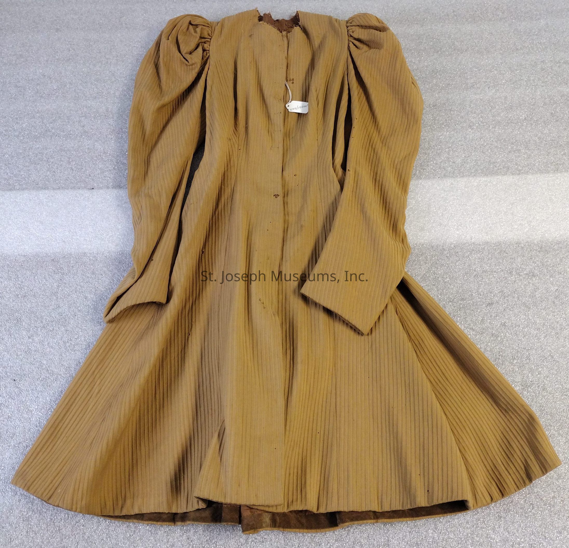 The image shows an old-fashioned, brown, long-sleeved dress with a high neckline and puffed shoulders, spread out on a flat surface. The fabric has vertical stripes, adding texture to the piece. The dress appears to be made of a heavy material, suggesting it may have been designed for cooler weather. There is no label or tag.