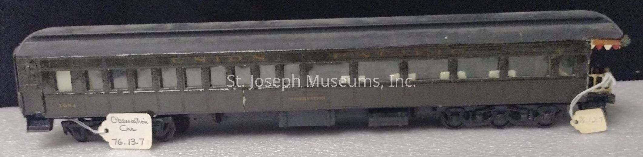 The image depicts a model of an old-fashioned train observation car, labeled as "Observation Car 76.13.7" with the number "1094" on its side. The car is painted in a dark hue and features a row of windows along its side beneath the lettering "UNION PACIFIC." It exhibits intricate detailing, including small, fine elements that mimic the features of a full-sized train car, giving it a realistic appearance despite its miniature scale. The model sits atop a textured surface, possibly for display or photography purposes.