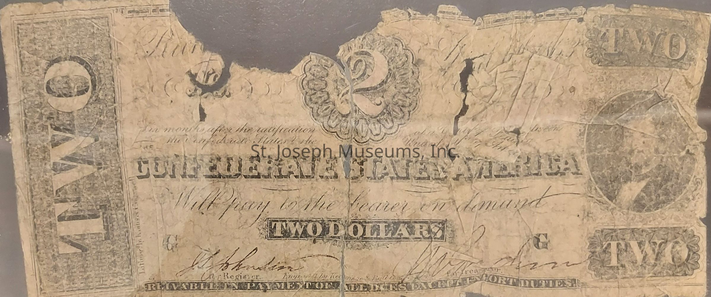 This image features an old, worn Confederate States of America two-dollar bill, showcasing significant signs of wear and tear, including creases, tears, and faded areas. The bill prominently displays the denomination "TWO" in large lettering along the sides and bottom corners. In the center, the words "Confederate States of America" are printed in bold, underlined text. The middle of the bill bears the designation "TWO DOLLARS" within a bordered box. Surrounding these elements are intricate, decorative engravings, along with various handwritten signatures and inscriptions, which contribute to the historical and aged appearance of the artifact.