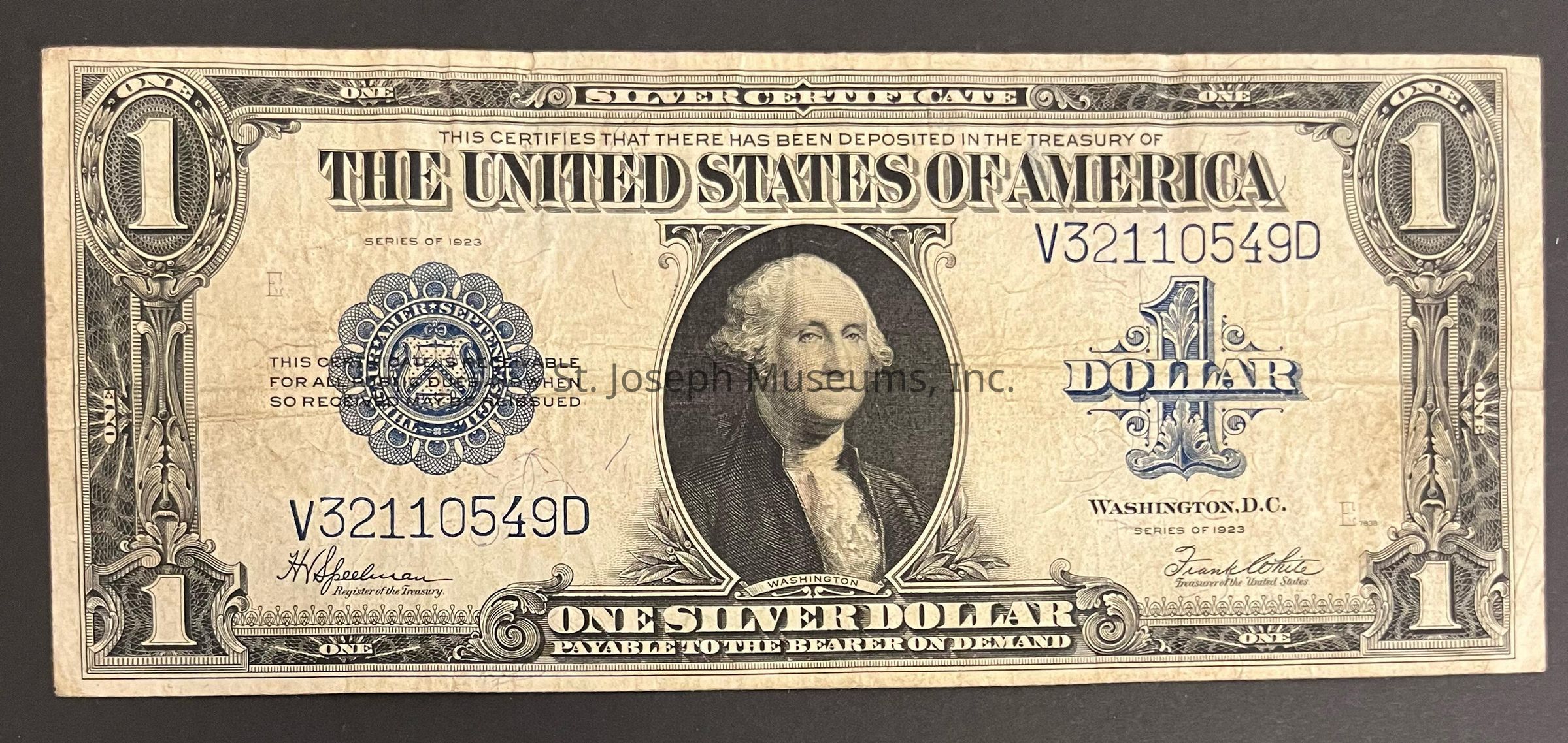 The image shows a vintage $1 Silver Certificate from the United States, issued in 1923. Centered at the top is "THE UNITED STATES OF AMERICA" with the serial number "V32110549D" to the right. The note prominently features an engraved portrait of George Washington inside a circular frame on the right side. Flanking Washington, intricate designs embellish the certificate, highlighting the artistic detail common in currency from this era. On the left side, a blue seal and serial number are visible. A large "1" appears in ornate typography on each corner. Notably, the text at the bottom states "ONE SILVER DOLLAR PAYABLE TO THE BEARER ON DEMAND," emphasizing its historically significant guarantee. The signatures of the Register of the Treasury and the Treasurer of the United States are present at the bottom, authenticating the note.