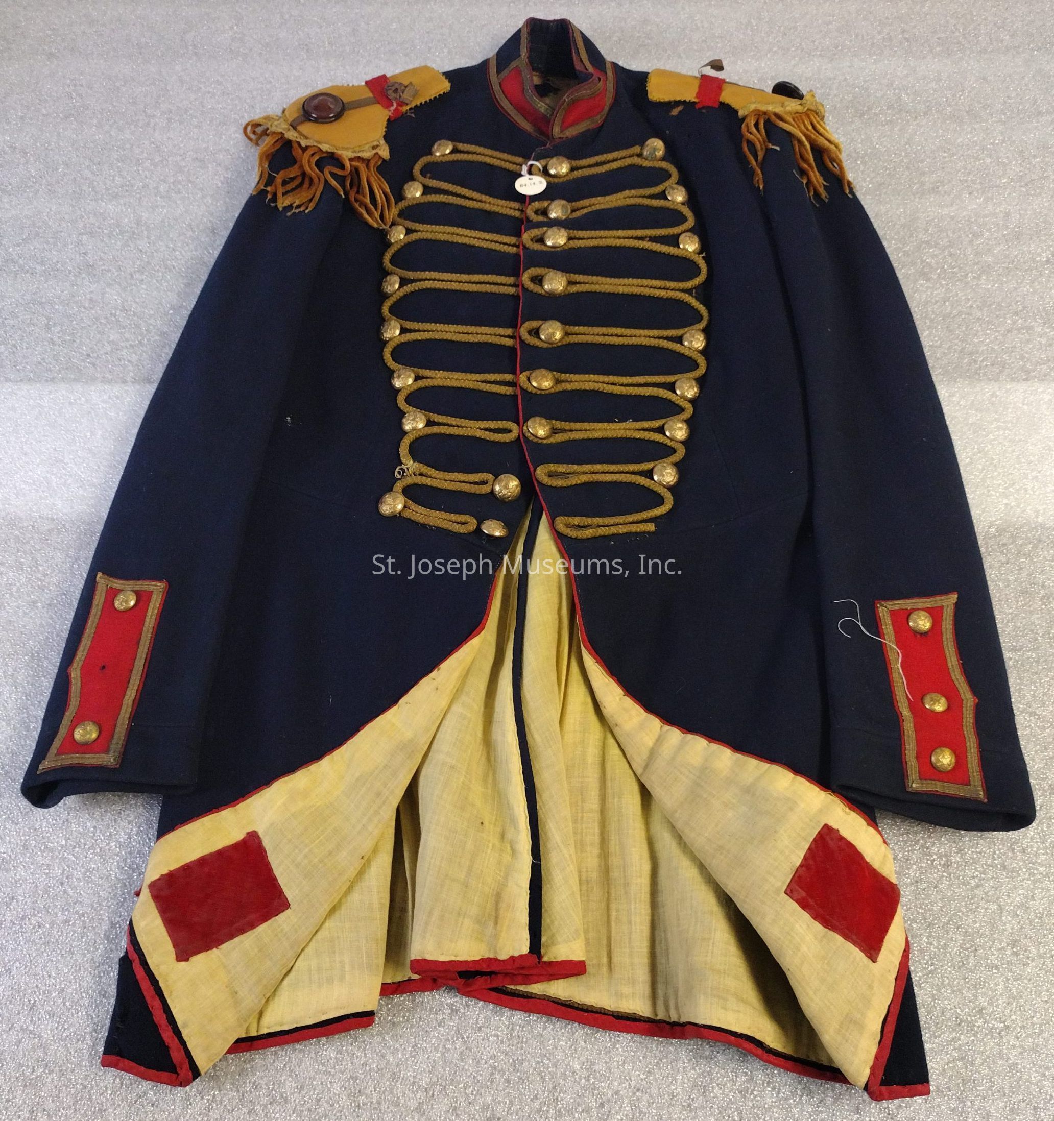 The image depicts a dark blue coat featuring red and gold trim, with gold cloth epaulettes adorned on each shoulder. The front of the coat is styled to be turned back, revealing a white lining accented by red velvet patches. On each sleeve cuff there is a red cloth patch, with three buttons fastening it securely. The front of the coat is embellished with nine rows of gold buttons and decorative gold braid.
