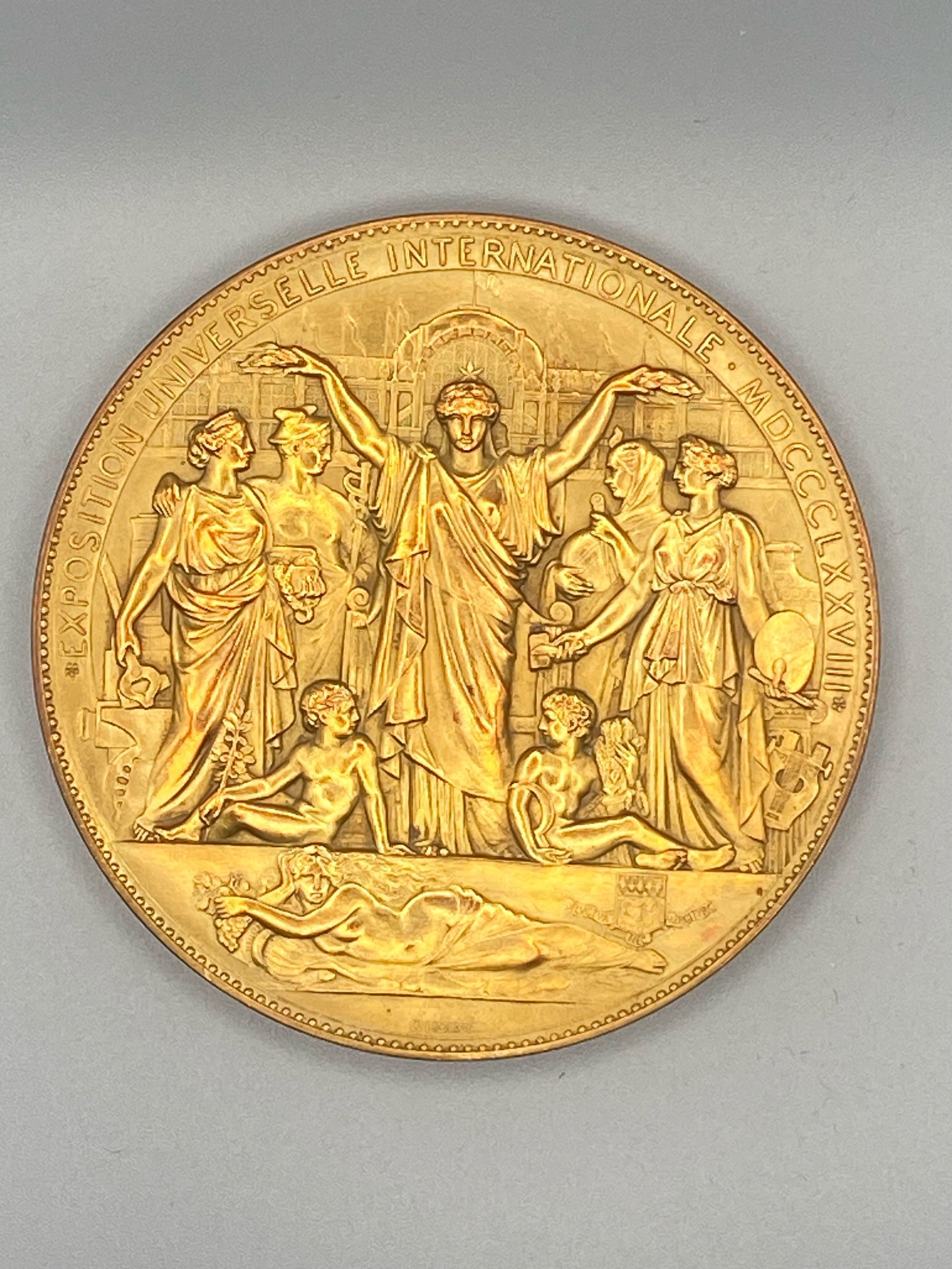 Obverse: The central figure on the obverse with the star on her head and a wreath in each hand seems to represent the notion of prize-giving. From left to right are figures of Industry, Commerce , Science , and the Arts. Below are two boys, one holding a branch and the other wheat and a scythe. In the background is a view of the exhibition and below a reclining river goddess (the Seine) and a shield bearing the arms of Paris. See text for further explanation.