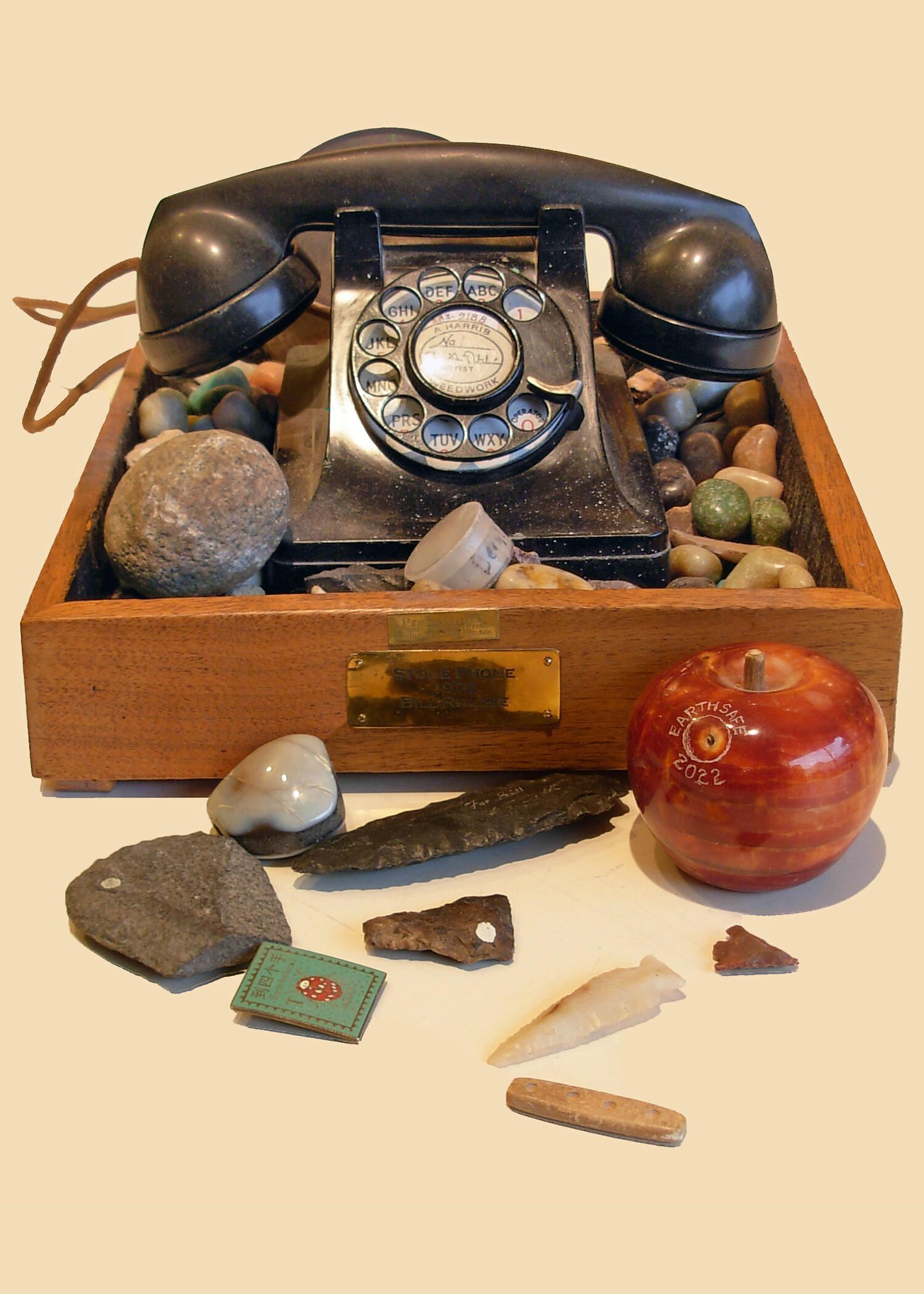 Stone phone with samples: A vintage telephone (ca. 1941) nested in a box of stones, primitive objects, memorabilia, CD/ROM printing plate, etc. the artist conceived to express "action-at-a-distance." The arrow points, for example, are the hunter's way to have an effect far from his each. In a way similar to paintings on the walls of prehistoric caves alongside handprints these are expressions, or explications, of actions at a distance almost unique to human beings. However, other creatures exhibit similar skills. Crows and monkeys use tools. Bowerbirds do marketing by adorning their bowers. The artist in this instance demonstrated his ability to transcend time and space with his telecom works in the early 1970s with "Dial-A-Teacher" and "Dial-An-Artist" projects, and, in its last interation, his installation in the restaurant of his friends, Kathy Fridstein and Mark Manley.