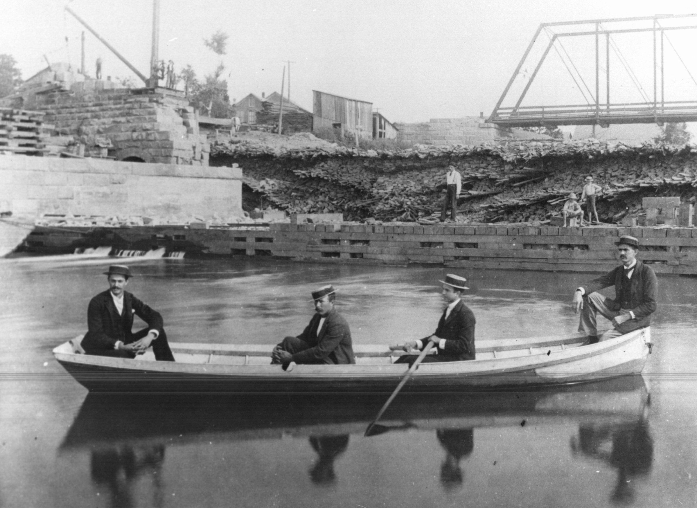 Muskingum River State Park - The Dover Brothers of Stockport, ca. 1880: The Dover Brothers pose for a photograph on a paddle boat on the Muskingum River. They owned and operated the Stockport Mill in the river town of Stockport near Lock #6. In the photograph's background, bystanders face the camera who are perhaps employed by the lumber industry. Note the stacks of timber behind these onlookers.