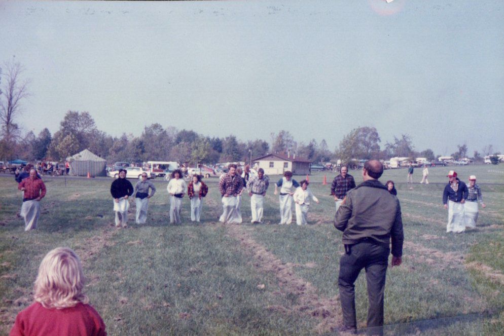 Indian Lake State Park - Sack Race, date unknown: Parkgoers at Indian Lake State Park participate in a sack race. During this event, participants stand in a large sack that comes up to their waist. This sack prohibits movement, which makes participants comically hop, jump, and fall over on their way to the finish line. The winner is the first person to hop across the finish line.