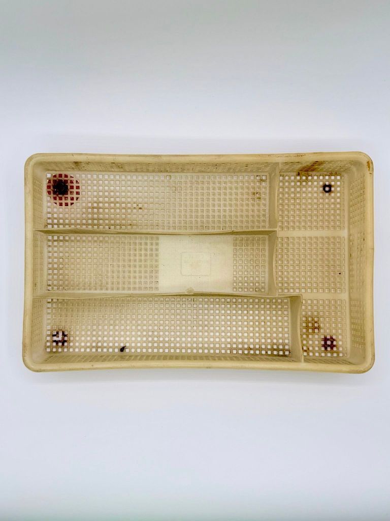 Perforated plastic compartment tray, repurposed as a dish drainer with bottle-cap feet
