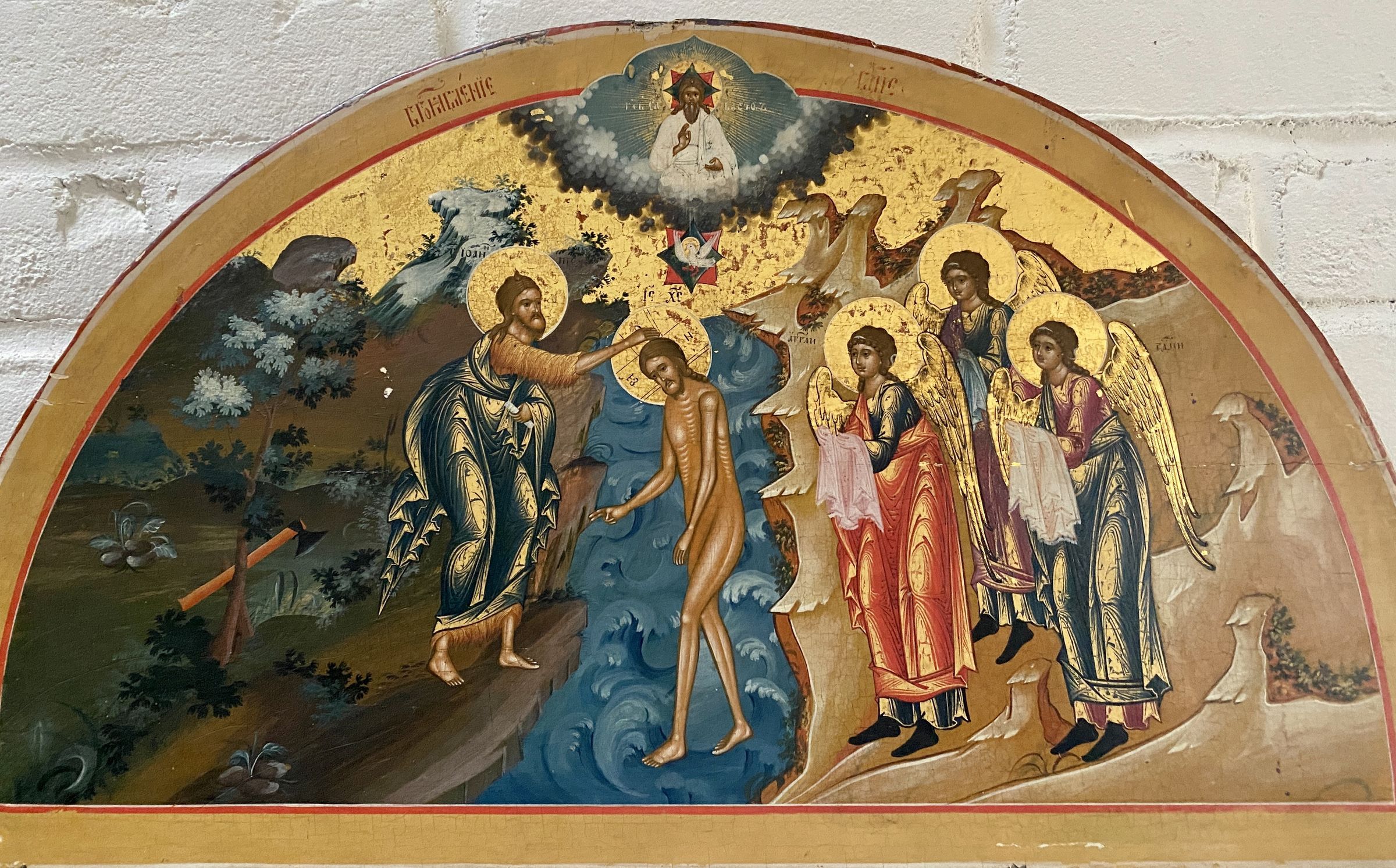 This semi-circular icon depicts a theophany (baptism): Jesus standing in flowing water, with John the Baptist’s arm outstretched over his head. They are accompanied by three angels, while overhead, the Father is portrayed within a cloud, gazing benevolently downwards, as the Holy Spirit, in the likeness of a dove, descends against a golden sky.