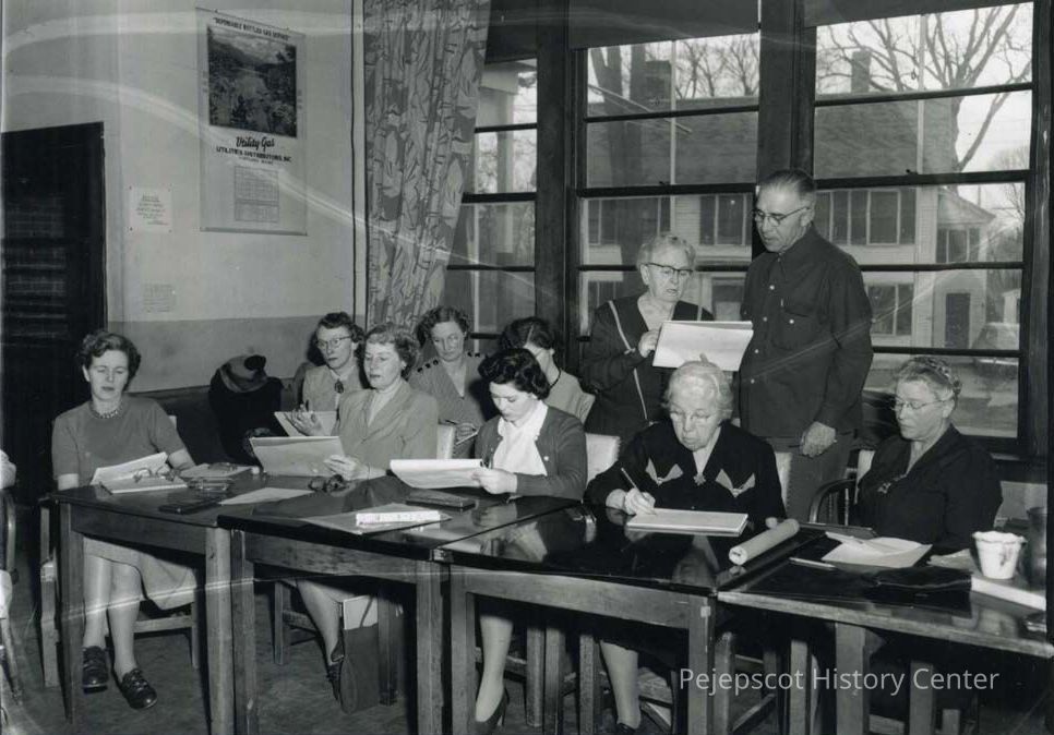 Art Lessons at the Brunswick Recreation Center: A black and white photograph of the creative arts group at the Brunswick Recreation Center, Brunswick., Maine. They were sponsored by the American Association of University Women. Eight women are sitting at the tables holding pencils and sketching pads focusing on their work. Miss Helen Varney stands at the back of the room talking to a man and directing the class.
Undated.