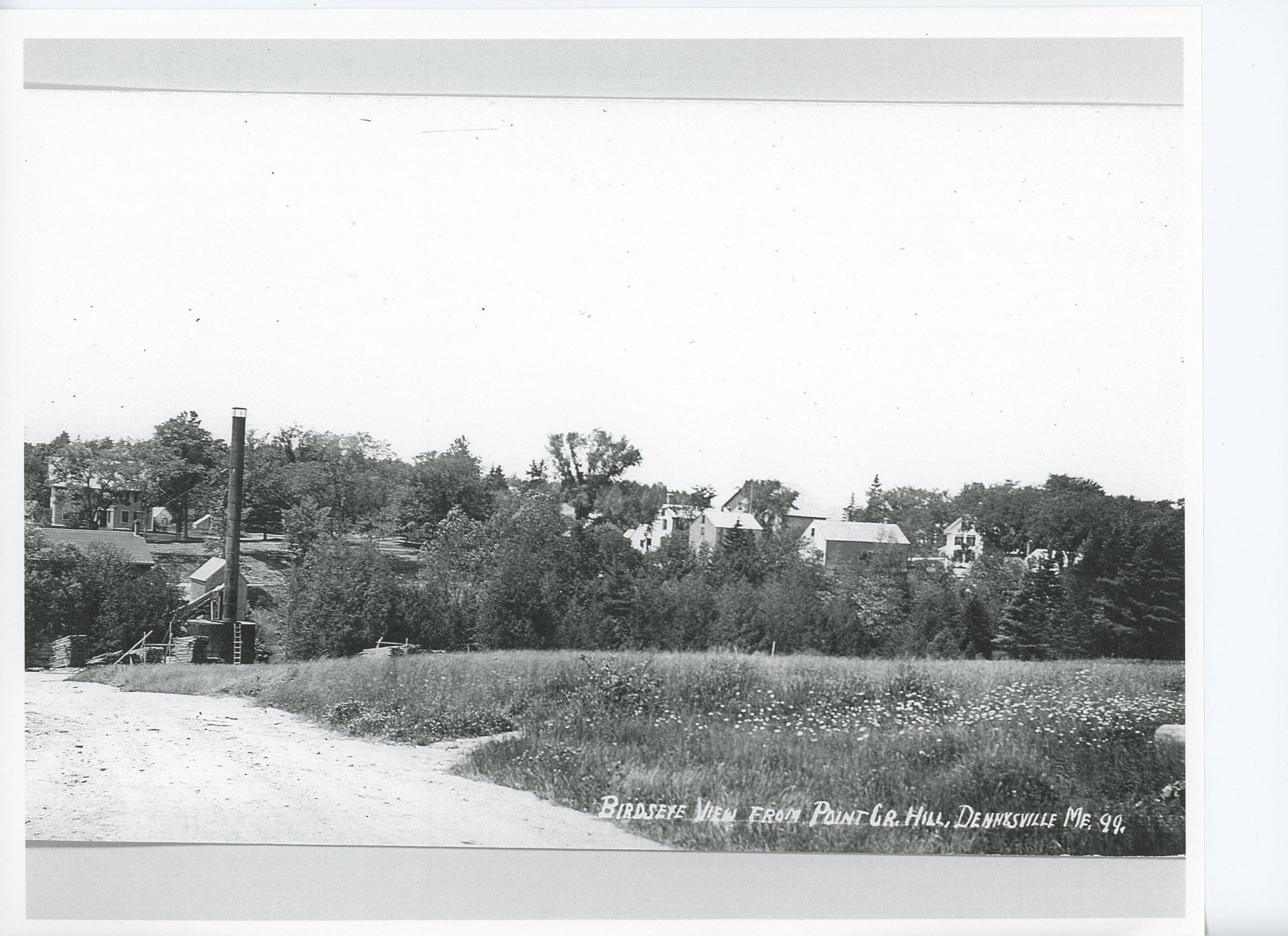 View of Dennysville from Lyons Hill Road in Edmunds.; The Dennys River Lumber Company Mill and waste burner are at the bottom of the hill with the mill manager's house on the hillside beyond. the buildings on store Hill are visible on the right in this image from around 1910.