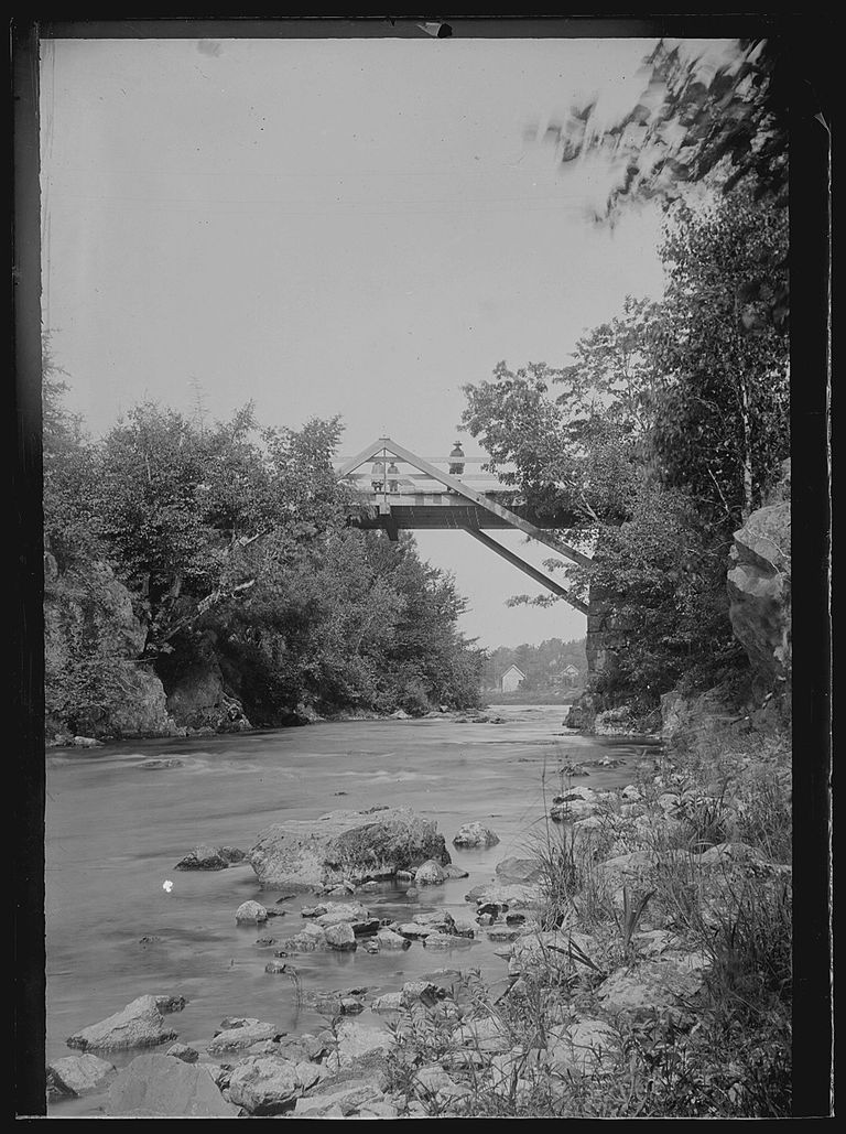          Falls Bridge over the Dennys River, c. 1885; Nineteenth century view of the Falls Bridge over the Dennys River, with several bystanders on the bridge, looking upstream towards houses along the Milwaukee Road in Dennysville visible in the distance.  The photograph was taken by Dr. John P. Sheahan in the 1880's.
   