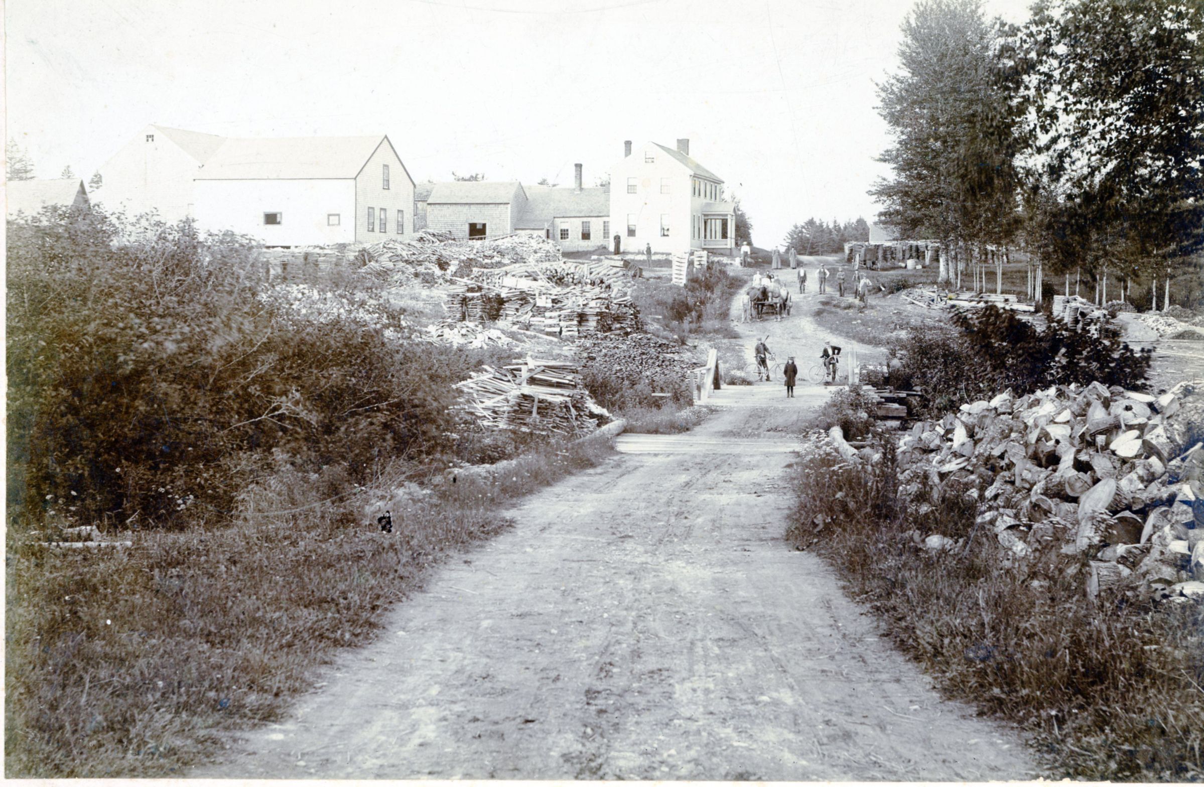 Bridge over Cathance Stream, next to Kilby and Smith's Sawmill, Marion, Maine; Lumber, boards and refuse piled next to the J.C. Allan House, later belonging into B.L. Smith, on the County Road over Cathance Stream in Marion , Maine, c. 1880. The pile of short pieces to the right were saved for making shingles at the mill on the downstream side of the bridge.