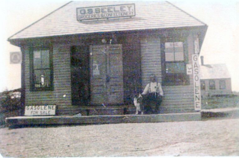          G. Stillman Seeley's Store, Edmunds, Maine; Advertising groceries and confectionery, as well as gasoline for sale, Stillman Seeley appears sitting on the porch with his own faithful companion.
   