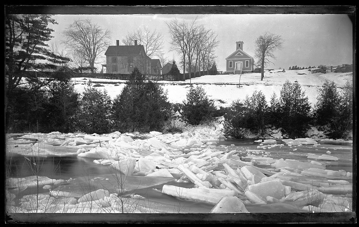 Ice Jam on the Dennys River with the Congregation Parsonage and Vestry; This image of ice choked Dennys River, was taken by John P. Sheahan of Edmunds in the 1880's. The Congregational parsonage, built in 1861 is to the left, while the Vestry on the right was used by the Church for Sunday School, services, suppers and other gatherings.