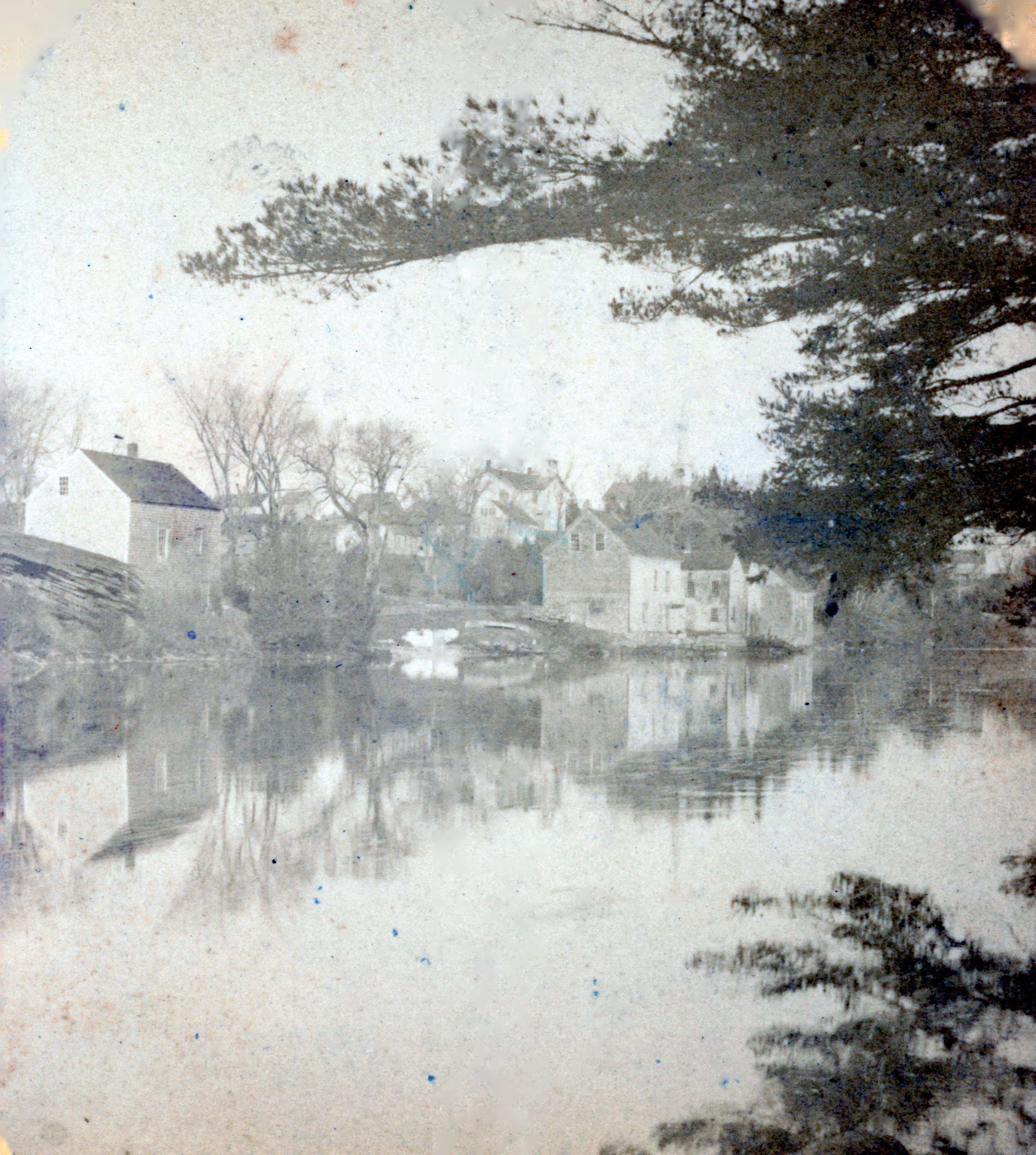 Shops and stores on the banks of the Dennys River, Dennysville, Maine.; D.K. Hobarts Drugstore is on the left, while Gardner's General Store and other shops line the bank of the Dennys River in this image taken around 1890 in Dennysville, Maine. The Town Schoolhouse and the steeple of the Congregational church building are visible on the hill beyond. Photograph courtesy of the Tides Institute in Eastport, Maine.