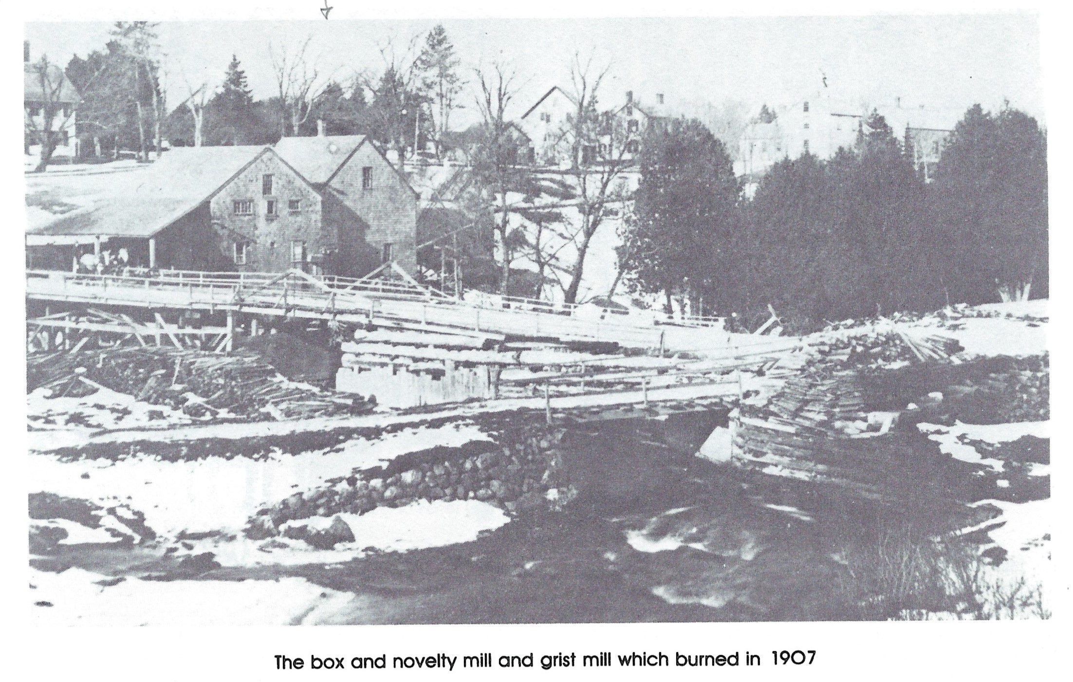 The Box and Novelty Mill and Grist Mill on the Dennys River, c. 1905; Water swirls under the Upper Bridge with the box and grist mills built by T.W. Allan on the far side of the Dennys River. Photograph reproduced from Rebecca W. Hobart, Dennysville 1786-1986 . . . and Edmunds, Too!