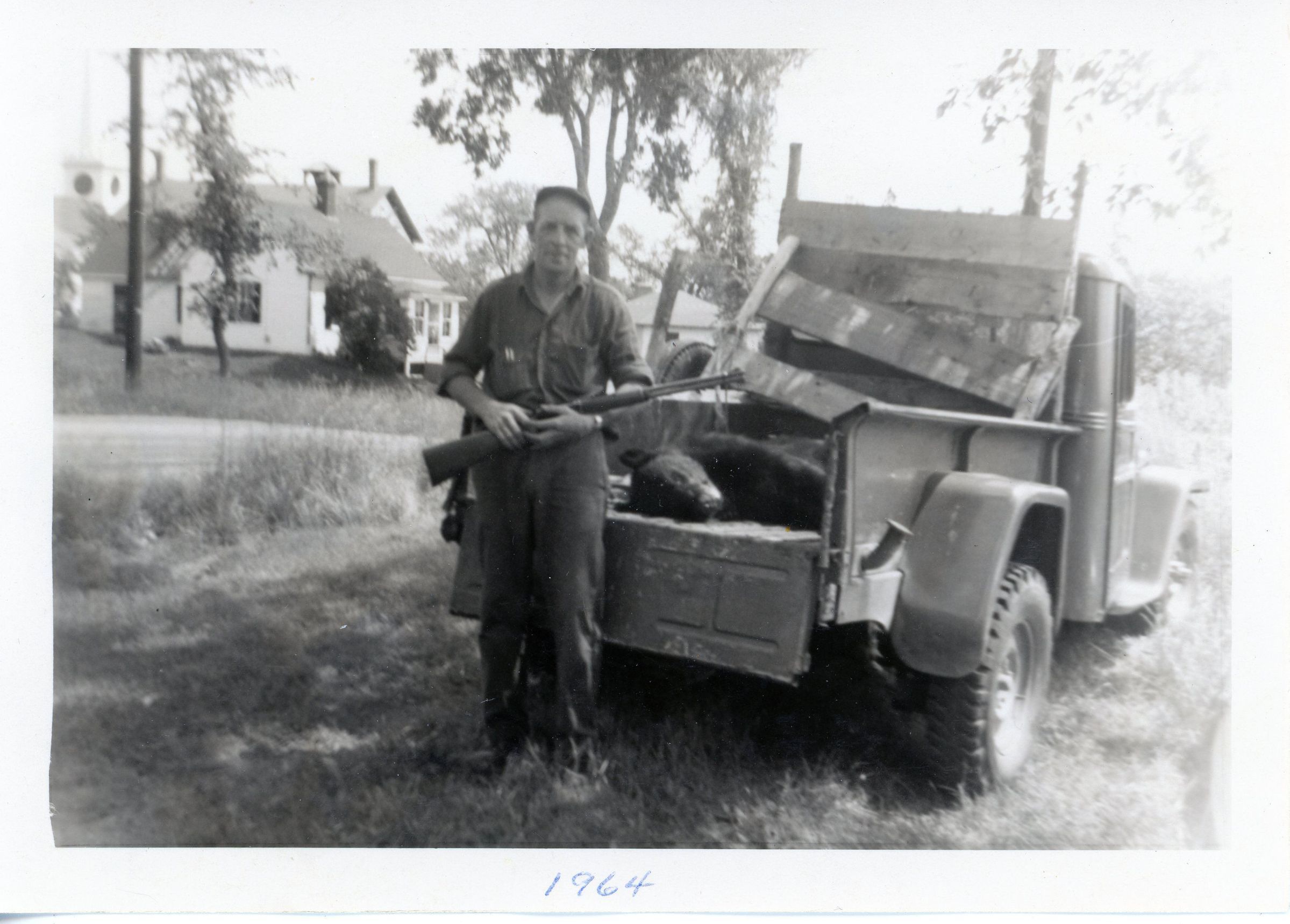 Forrest Leighton, July 4th, 1964, Dennysville, Maine; Forrest Leighton is photographed with a black bear at his house on King Street in Dennysville Maine. Behind can be see the roof of the H.A.M. Jones House, the schoolhouse, and the Congregational Church's belfry and steeple beyond.,