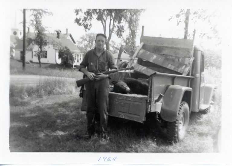          Forrest Leighton, July 4th, 1964, Dennysville, Maine; Forrest Leighton is photographed with a black bear at his house on King Street in Dennysville Maine.  Behind can be see the roof of the H.A.M. Jones House, the schoolhouse, and the Congregational Church's belfry and steeple beyond.,
   