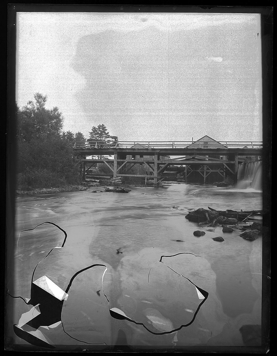 Upper Bridge of the Dennys River, by John P. Sheahan, c. 1885; Photographic image of the Upper (upstream) Bridge below the Lincoln mills on the Dennys River. The sluice is on the right-hand or Dennysville side of the river, with the State Seal pines on the Edmunds shore to the left. The photographer, Dr. John Parris Sheahan of Edmunds, has contrived to photograph his horse and buggy on the bridge of the left of the lath and shingle mill. This bridge is documented by Rebecca Hobart in her town history as being constructed by agreement of both communities in 1836.