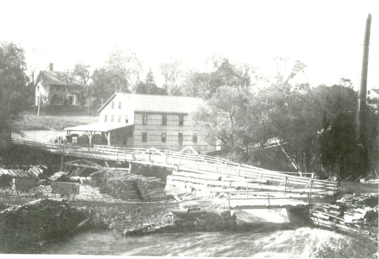          Dennysville Lumber Company in Dennysville, Maine; Water sluices around the mill dam, which powers the newly rebuilt lumber mill  in 1907, with the Mill House. where the company managers lived on the hill beyond.  A waste burner with conveyor belt stands on the Edmunds side of the river to consume the refuse of the mill.
   