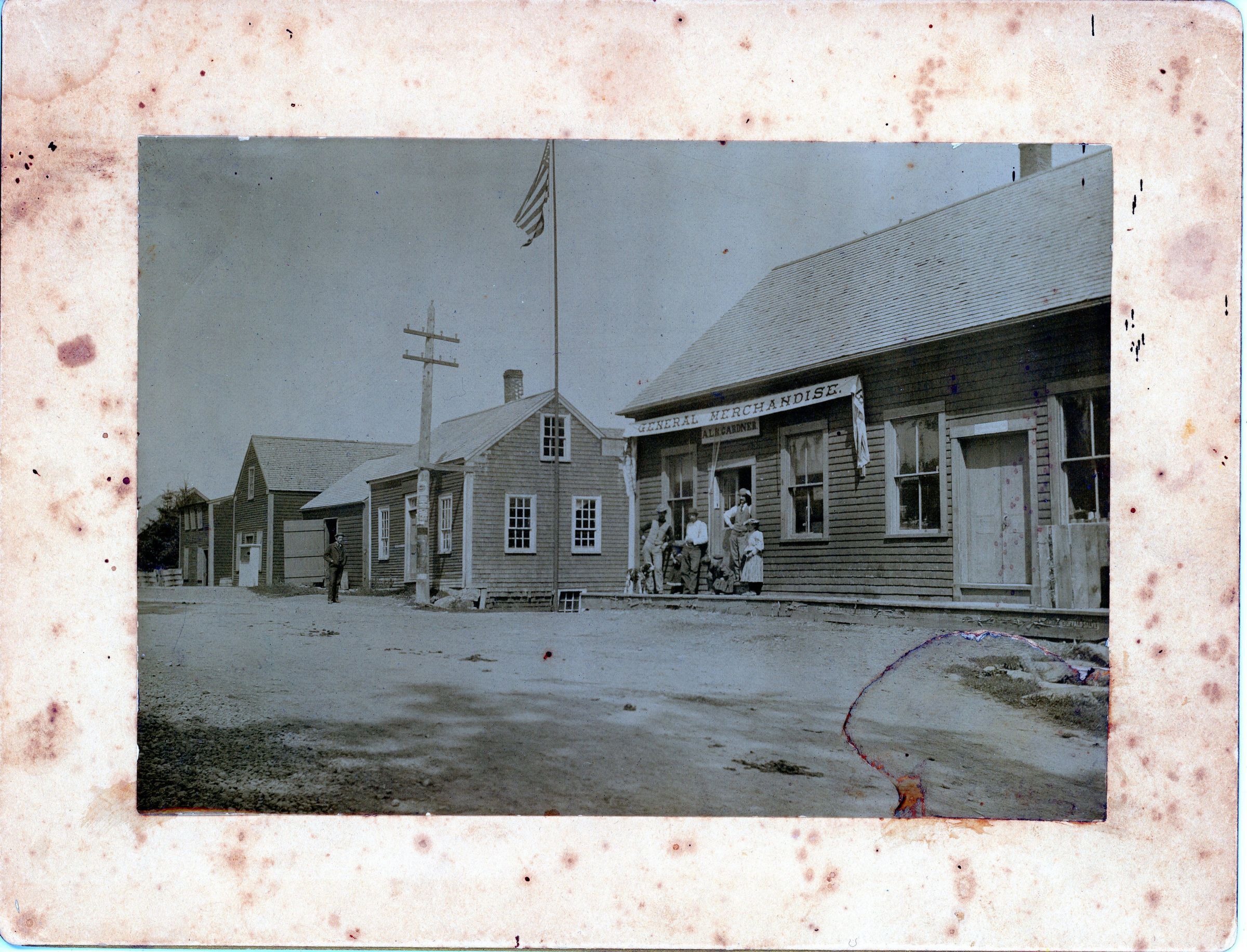 Early View of the A. L. Gardner Store, Dennysville, Maine in 1900; Beyond the A.L.R. Gardner store advertising General Merchandise in the foreground are McLauchlin's shoe store, another store, a carpenter shop and the blacksmith shop, originally built by William Kilby.