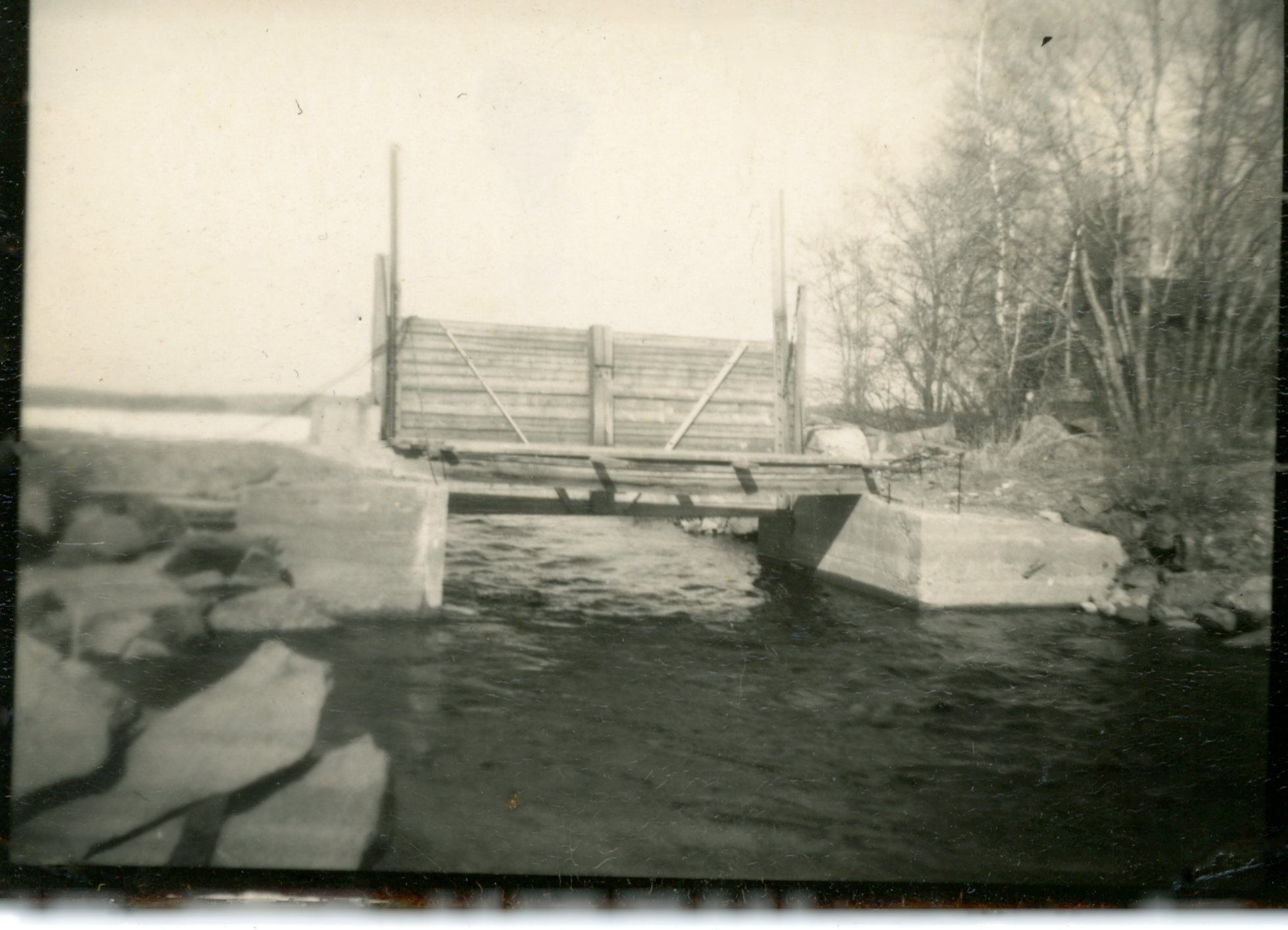 Dam at the head of the Dennys River on Meddybemps Lake, c. 1960; Water from Meddybemps Lake flows under the raised gate of the dam at the head of the Dennys River in Meddybemps, Maine.