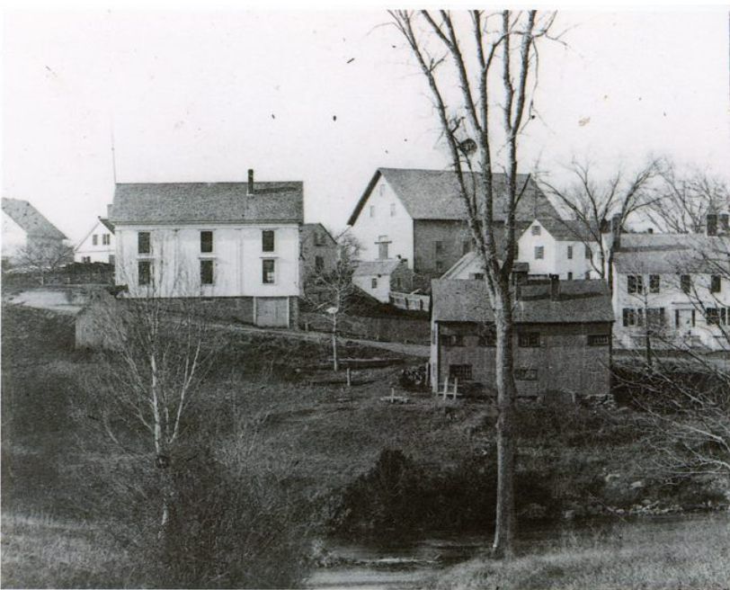 Shops and businesses on Store Hill in Dennysville, c. 1890.; Lyman K. Gardner's blacksmith shop occupies the center of this image on the banks of the Dennys River as seen from the Edmunds side of the river.