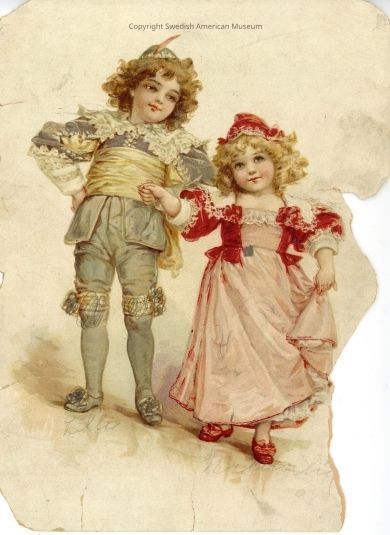 2003.19.2_PDF: The boy is dressed in a gray suit with gray socks and gray shoes. The boy's jacket has white lace trim in the collar area, at the bottom of the sleeves and in the middle, where the buttons are. The girl is wearing a pink dress with a matching red jacket and a red hat, the latter of which has white embroidered flowers. The girl's dress has white lace trim in the collar area and her jacket has red and white lace trim in the collar area and near the bottom of the sleeves.